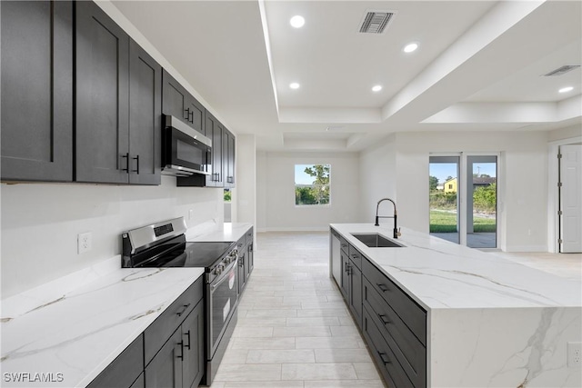 kitchen featuring a sink, visible vents, appliances with stainless steel finishes, light stone counters, and a raised ceiling
