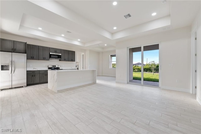 kitchen featuring a sink, a raised ceiling, stainless steel appliances, visible vents, and open floor plan