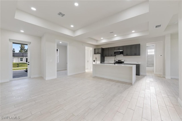 kitchen with fridge with ice dispenser, a tray ceiling, visible vents, light countertops, and open floor plan