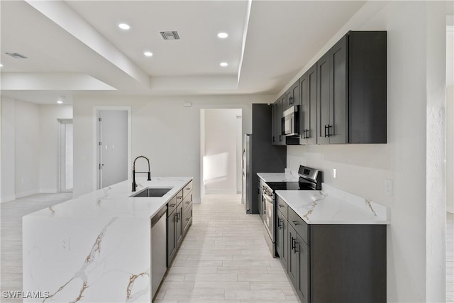 kitchen featuring a sink, a tray ceiling, stainless steel appliances, light stone countertops, and visible vents