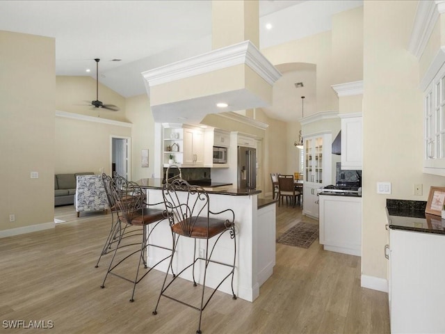 kitchen with dark countertops, a kitchen bar, open shelves, high vaulted ceiling, and appliances with stainless steel finishes
