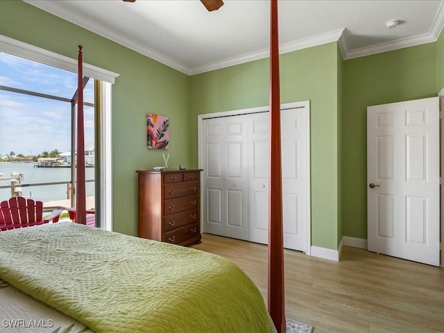 bedroom featuring light wood finished floors, a water view, baseboards, a closet, and crown molding