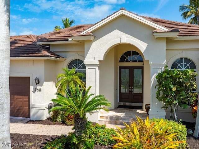entrance to property with french doors, a tile roof, an attached garage, and stucco siding