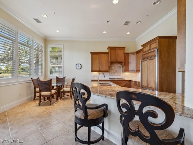 28561 Calabria Ct Unit 102, Naples, FL 34110 - kitchen featuring a sink, paneled built in fridge, brown cabinets, tasteful backsplash, and a breakfast bar