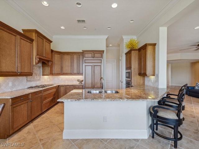 28561 Calabria Ct Unit 102, Naples, FL 34110 - kitchen featuring a sink, built in appliances, light stone countertops, a peninsula, and brown cabinetry