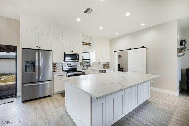 7717 16th Ter, Labelle, FL 33935 - kitchen featuring appliances with stainless steel finishes, a barn door, white cabinetry, a kitchen island, and decorative backsplash