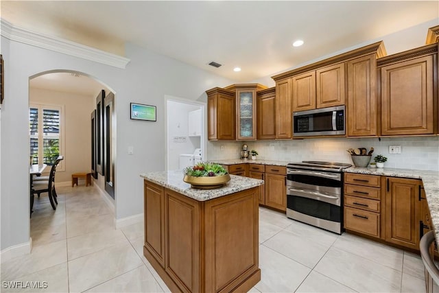 1518 Mcgregor Reserve Dr, Fort Myers, FL 33901 - kitchen with appliances with stainless steel finishes, brown cabinetry, arched walkways, backsplash, and a kitchen island