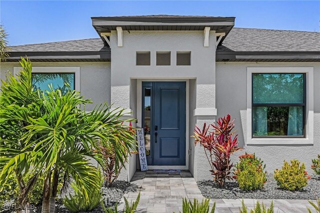 137 SE 23rd Ter, Cape Coral, FL 33990 - view of exterior entry featuring a shingled roof and stucco siding