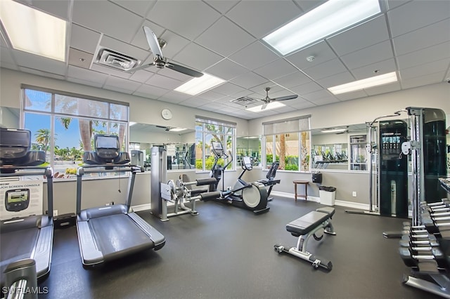 gym with a paneled ceiling, ceiling fan, baseboards, and visible vents