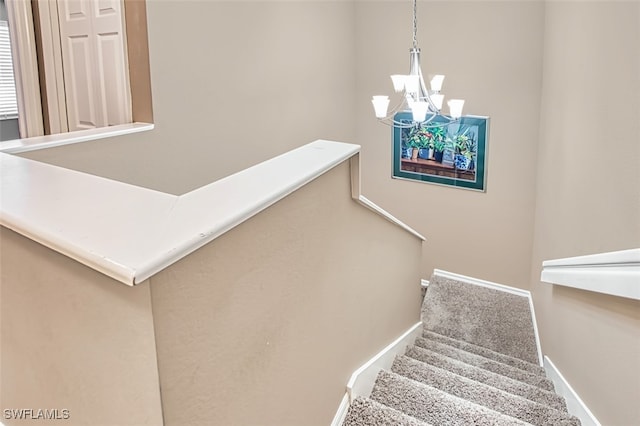stairs with an inviting chandelier, carpet floors, and baseboards