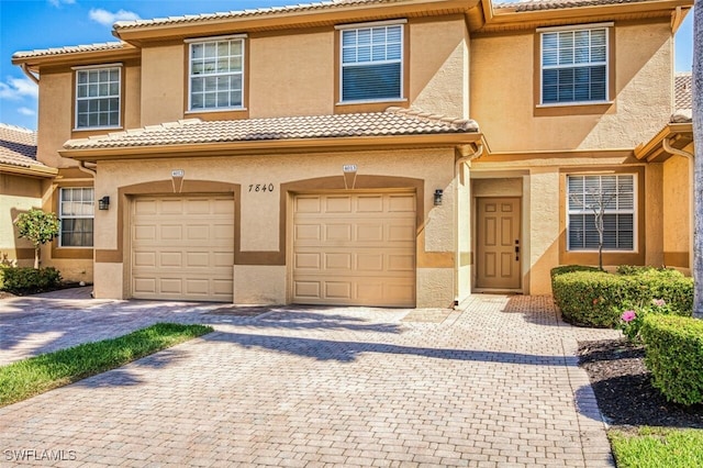 multi unit property with an attached garage, decorative driveway, a tile roof, and stucco siding