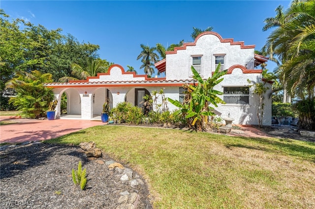 mediterranean / spanish house featuring a tile roof, a front yard, and stucco siding