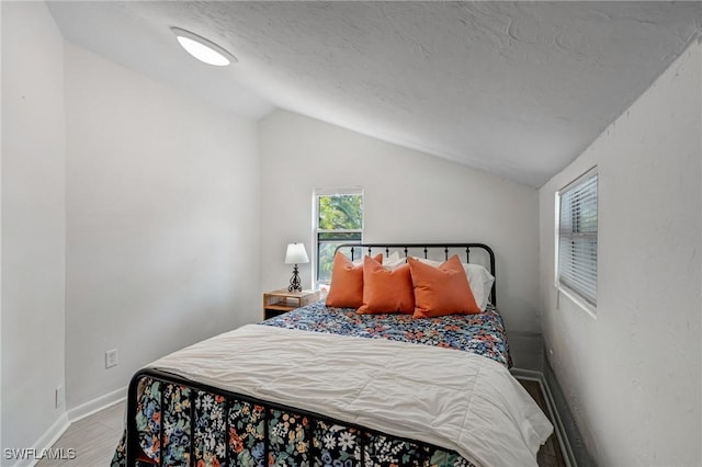 bedroom with baseboards, a textured ceiling, lofted ceiling, and wood finished floors