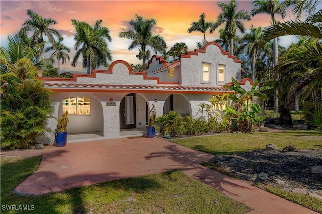 mediterranean / spanish house featuring a porch, a lawn, a tiled roof, and stucco siding