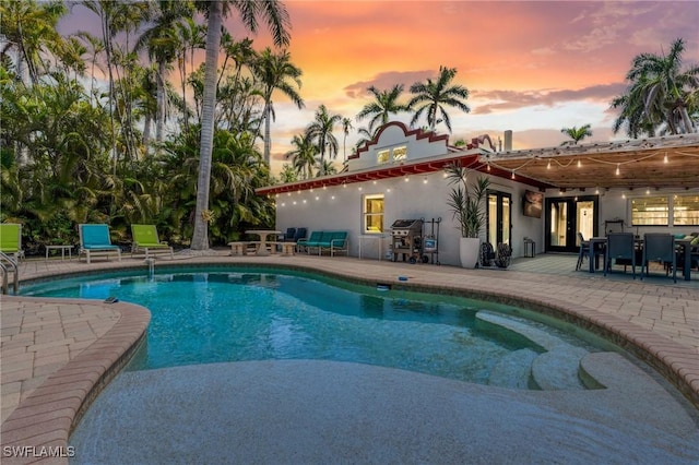 pool at dusk with a patio, an outdoor pool, french doors, and area for grilling