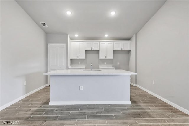 2609 59th St W, Lehigh Acres, FL 33971 - kitchen featuring an island with sink, a sink, wood tiled floor, white cabinets, and visible vents