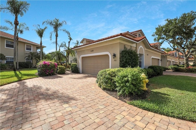 mediterranean / spanish house featuring a garage, a front lawn, stucco siding, and decorative driveway