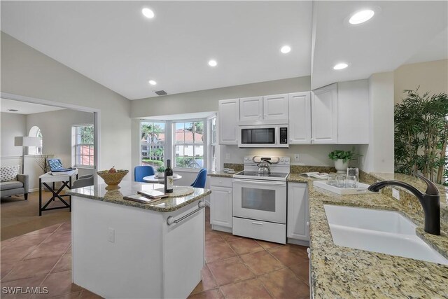 kitchen featuring light stone counters, vaulted ceiling, a sink, white appliances, and white cabinetry