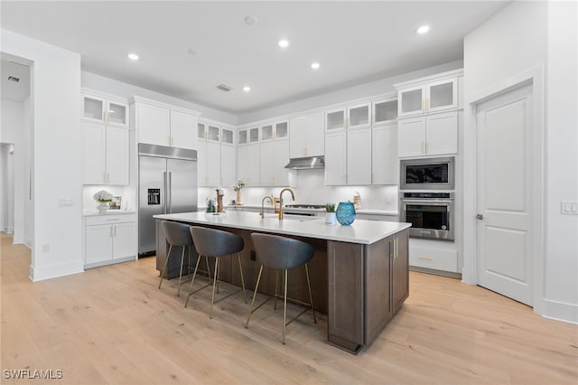 16214 Verilyn Cir, Naples, FL 34110 - kitchen with light countertops, light wood-style floors, a kitchen island with sink, a kitchen bar, and built in appliances