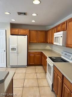 18301 Pine Nut Ct, Lehigh Acres, FL 33972 - kitchen with brown cabinetry, visible vents, white appliances, light countertops, and light tile patterned floors