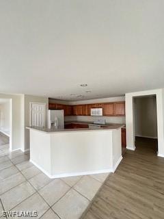 18301 Pine Nut Ct, Lehigh Acres, FL 33972 - kitchen featuring brown cabinets, a spacious island, baseboards, stainless steel fridge with ice dispenser, and white microwave