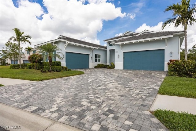 prairie-style house with stucco siding, decorative driveway, a front yard, and a garage