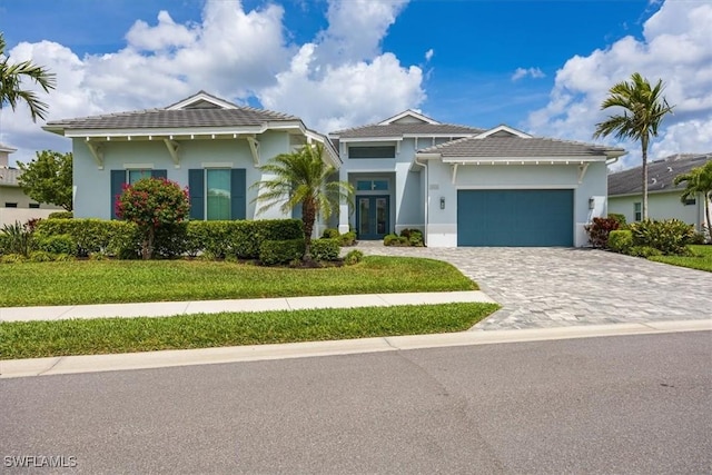 view of front of home featuring french doors, a front lawn, a garage, stucco siding, and decorative driveway