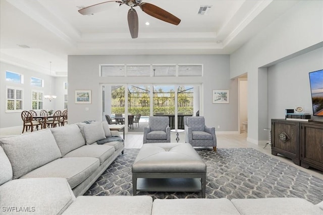 living room with ceiling fan with notable chandelier, baseboards, a high ceiling, visible vents, and a raised ceiling