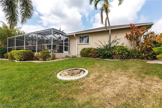 rear view of house with stucco siding, a lanai, and a lawn