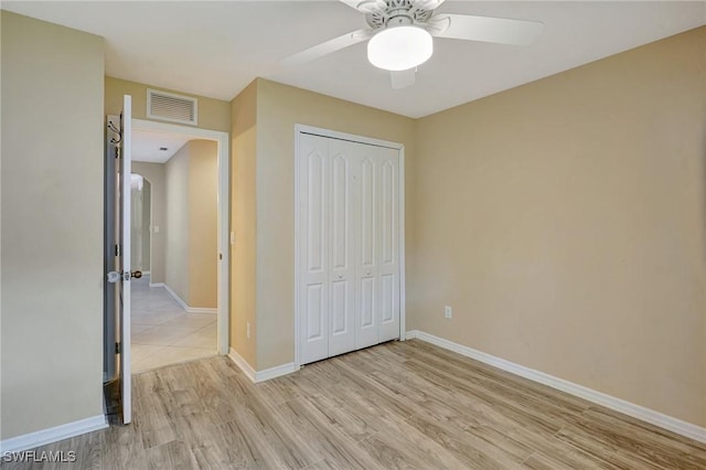 unfurnished bedroom with visible vents, a closet, light wood-style floors, baseboards, and arched walkways