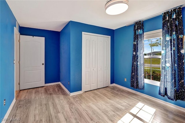 unfurnished bedroom with baseboards, wood finished floors, and a closet