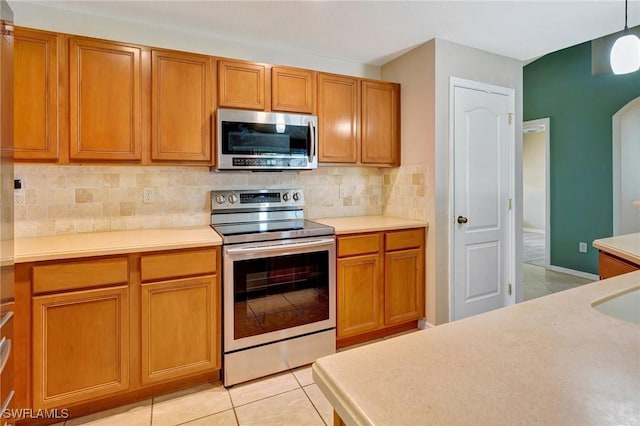 kitchen featuring brown cabinetry, tasteful backsplash, light countertops, light tile patterned floors, and stainless steel appliances