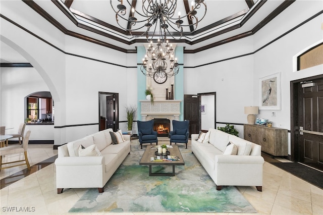 tiled living area with a towering ceiling, a warm lit fireplace, arched walkways, crown molding, and a chandelier