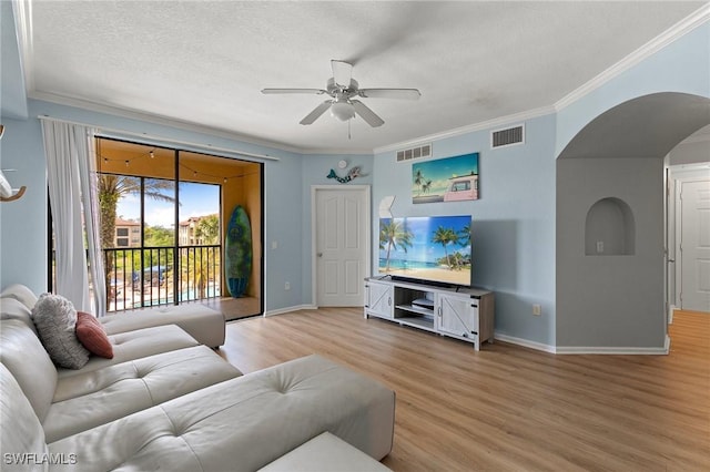 living room with arched walkways, crown molding, visible vents, and light wood-style flooring