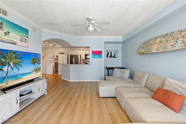 living area with arched walkways, light wood-type flooring, visible vents, ceiling fan, and ornamental molding