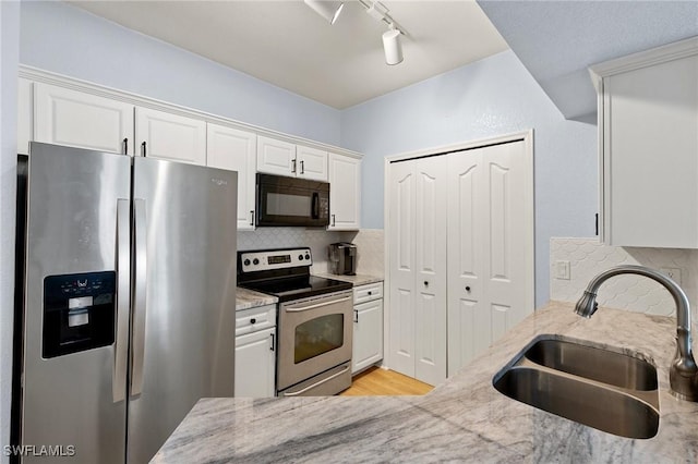 kitchen with a sink, tasteful backsplash, white cabinetry, light stone counters, and appliances with stainless steel finishes