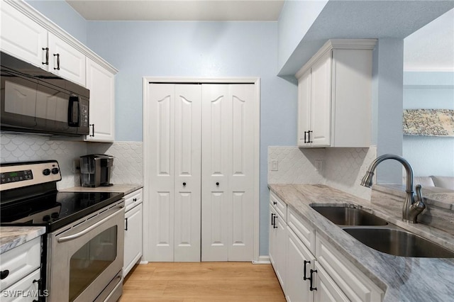 kitchen with backsplash, a sink, black microwave, light wood-style flooring, and electric range