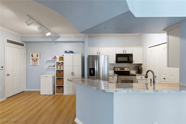 kitchen featuring light wood finished floors, a peninsula, light stone countertops, track lighting, and appliances with stainless steel finishes