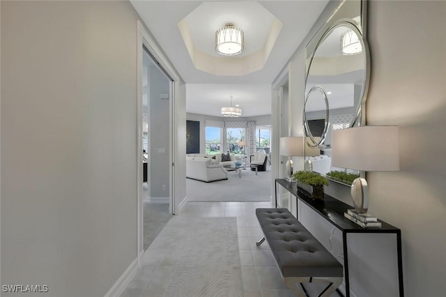 hallway featuring light tile patterned flooring, an inviting chandelier, light carpet, a raised ceiling, and baseboards