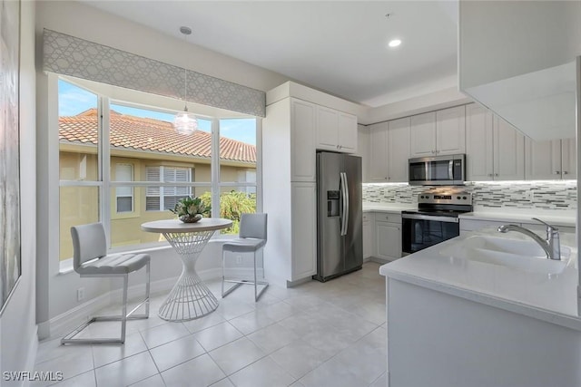 kitchen featuring backsplash, appliances with stainless steel finishes, a sink, light countertops, and white cabinets