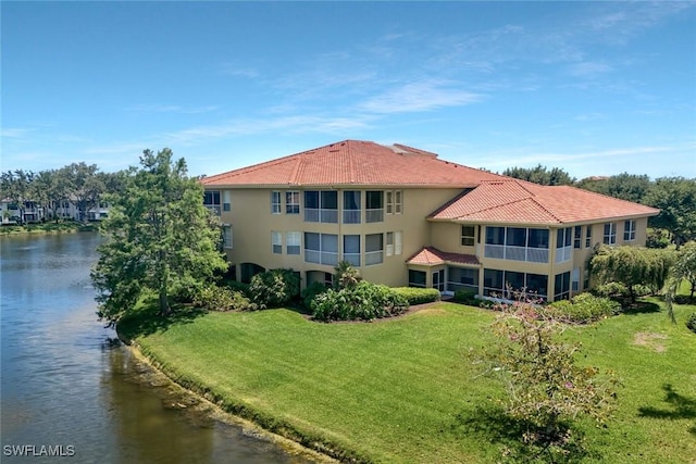 rear view of property with a lawn, a water view, stucco siding, and a tiled roof