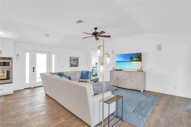 living area with vaulted ceiling, visible vents, a ceiling fan, baseboards, and light wood-style flooring