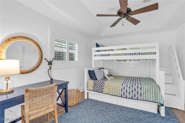 bedroom with ceiling fan, wood finished floors, and a raised ceiling