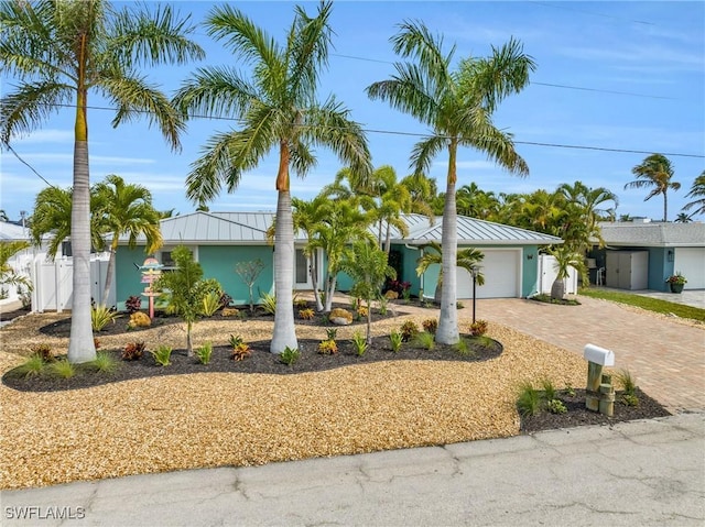 ranch-style home with a standing seam roof, metal roof, fence, a garage, and decorative driveway