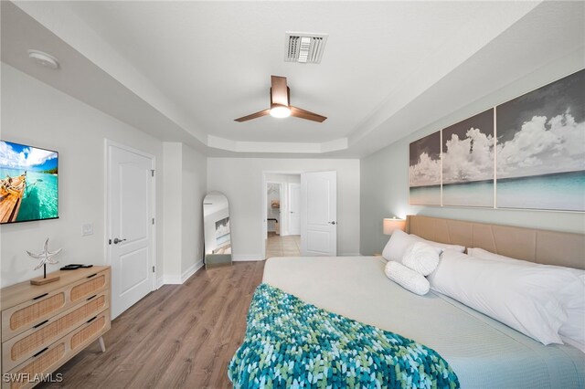 bedroom featuring wood finished floors, a tray ceiling, baseboards, and a ceiling fan