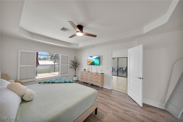 bedroom featuring a tray ceiling, baseboards, light wood-style floors, and a ceiling fan