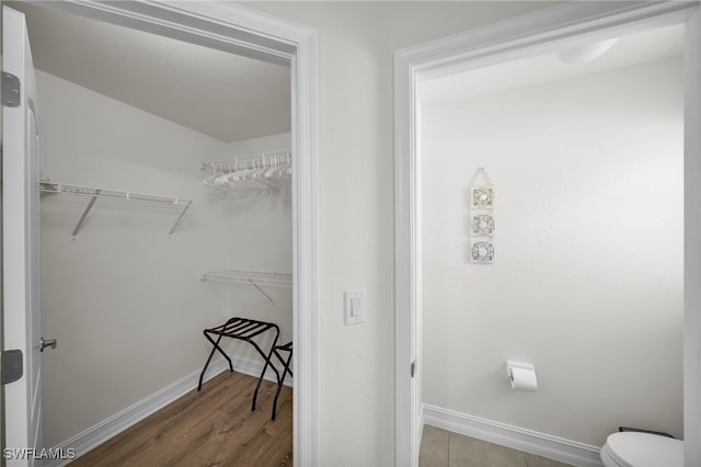 bathroom featuring baseboards, a walk in closet, toilet, and wood finished floors