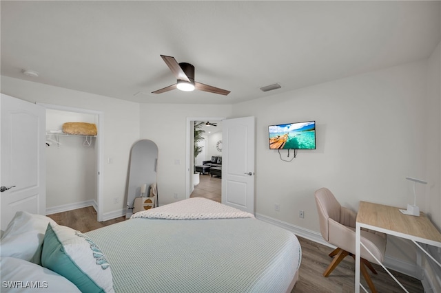 bedroom featuring ceiling fan, baseboards, a spacious closet, wood finished floors, and arched walkways