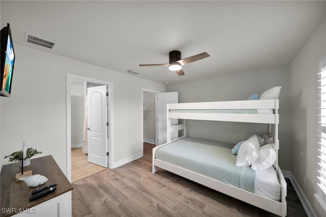 bedroom with light wood-style flooring, baseboards, a ceiling fan, and a walk in closet