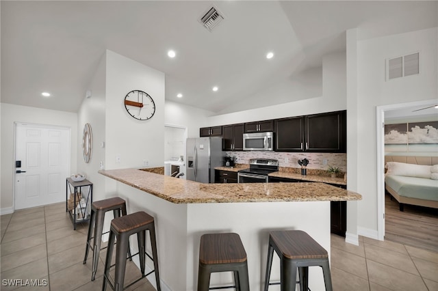 kitchen featuring stainless steel appliances, a breakfast bar area, vaulted ceiling, light tile patterned floors, and light stone countertops
